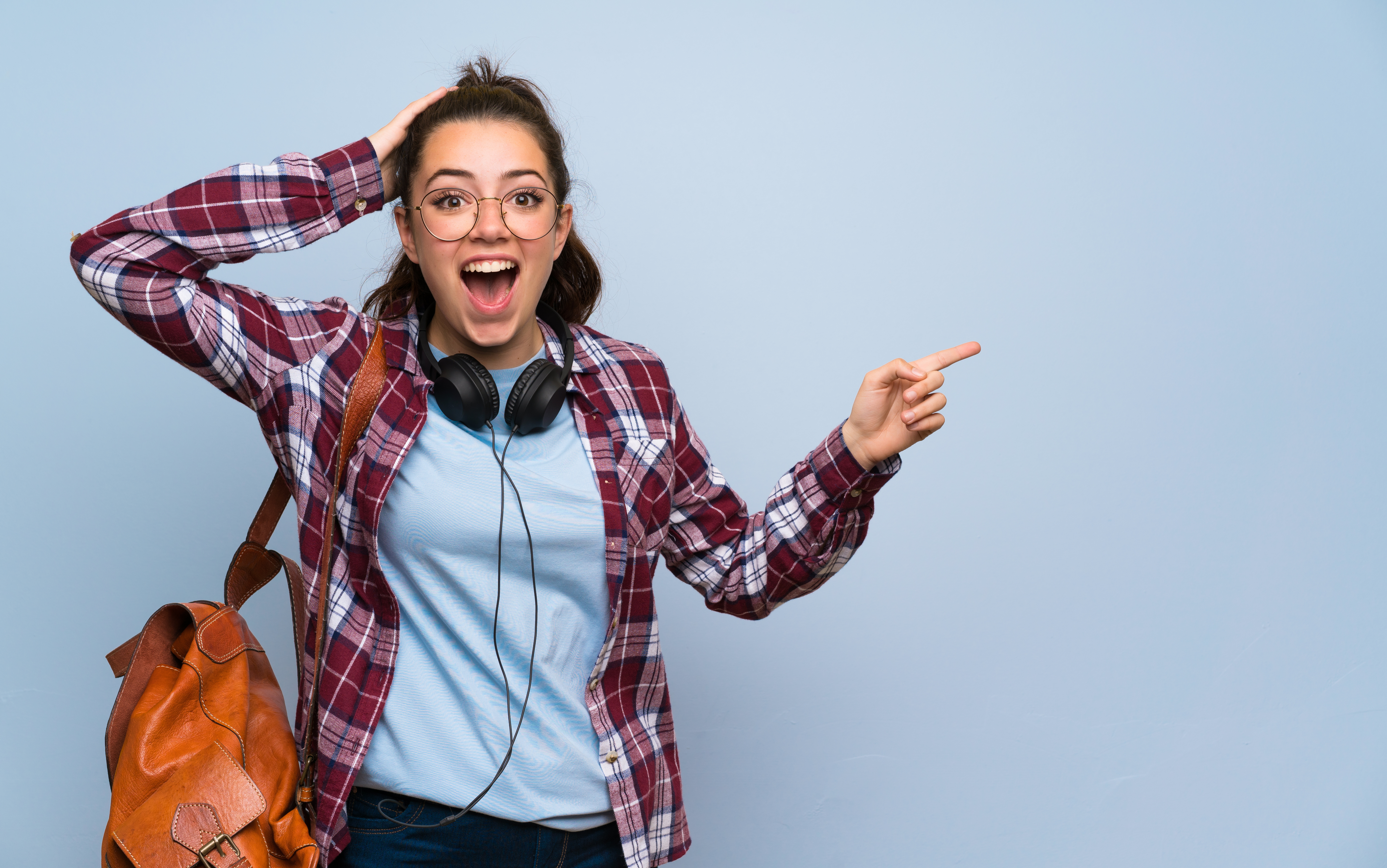 Teenager student girl over isolated blue wall surprised and pointing finger to the side