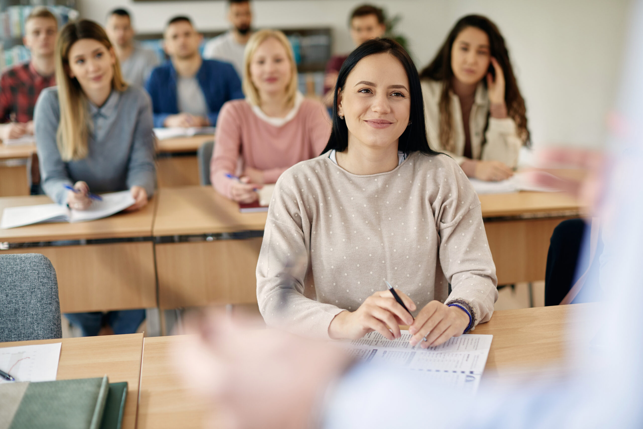 Smiling female student and her classmates listening teacher's lecture during a class at the university.